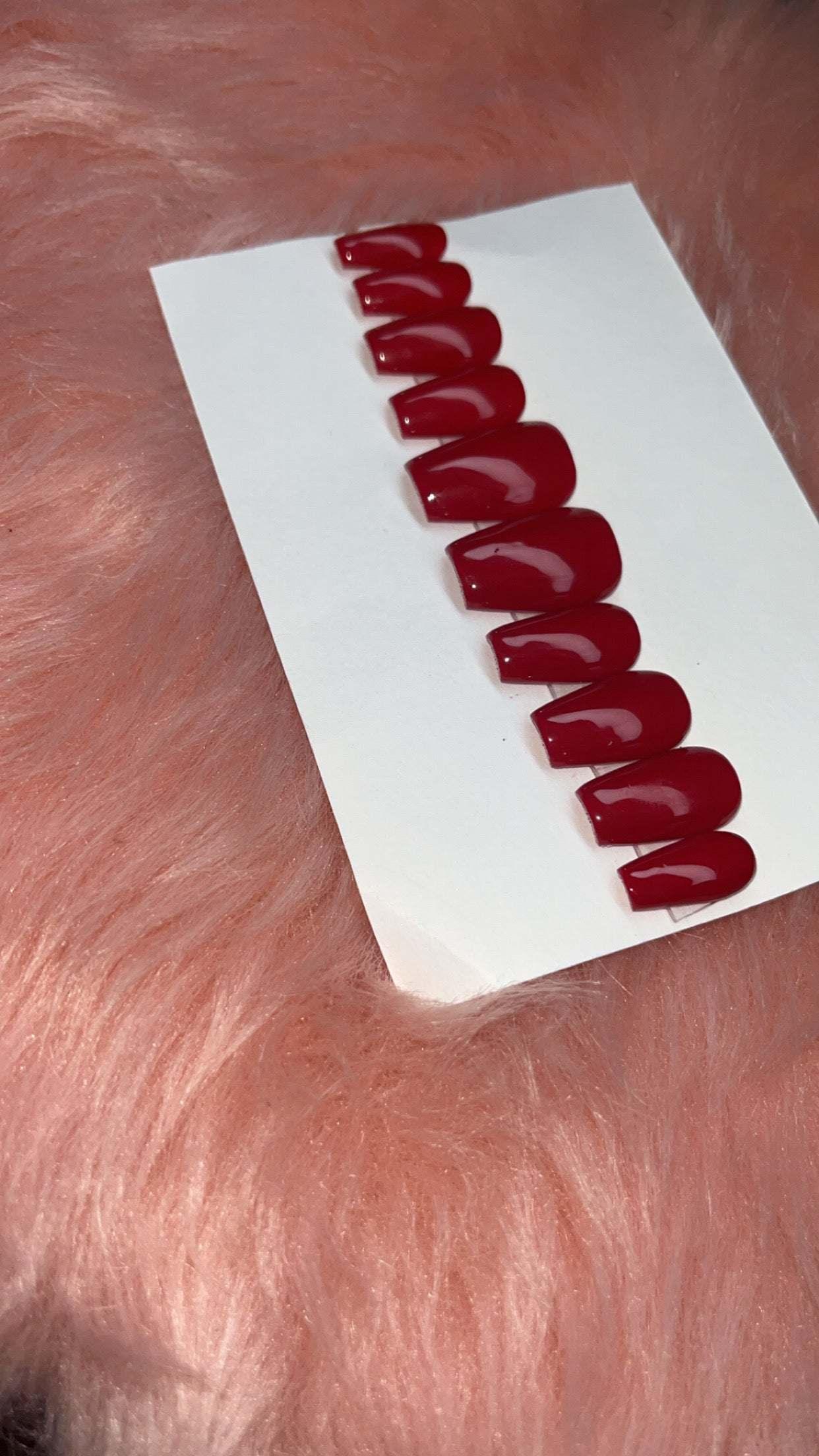 Set of glossy raspberry press-on nails arranged on white card over pink fur background