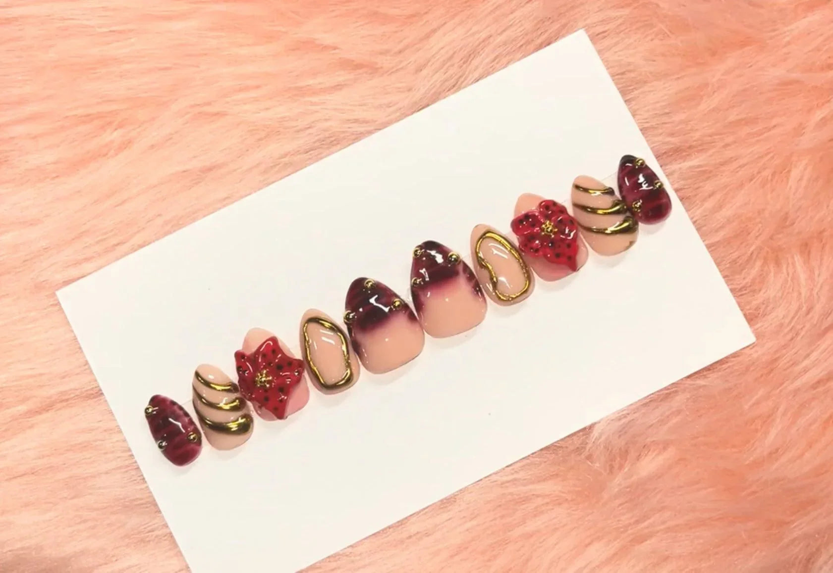 Red gold watermelon-themed press-on nails with black accents and floral details on a white card background