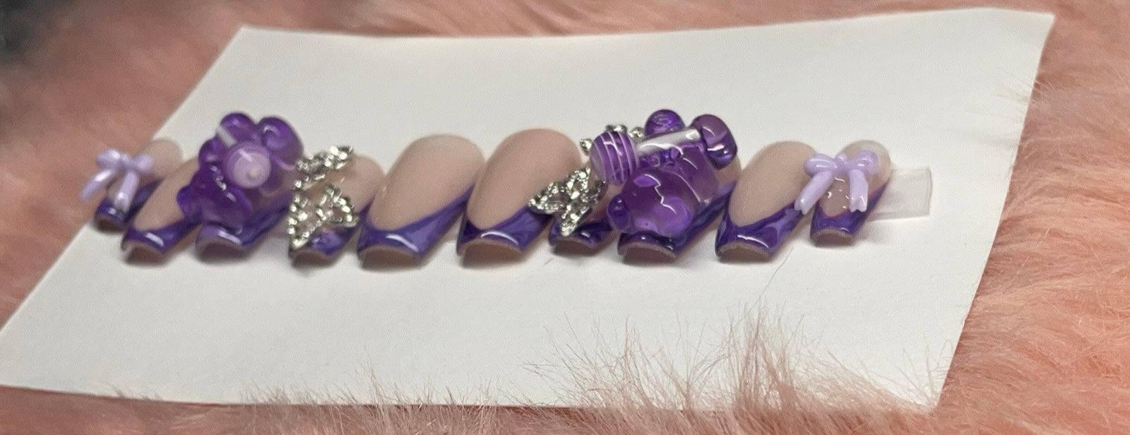 Purple "Taste the Burst" nail polish with 3D floral and bow nail art on artificial nails set on white card